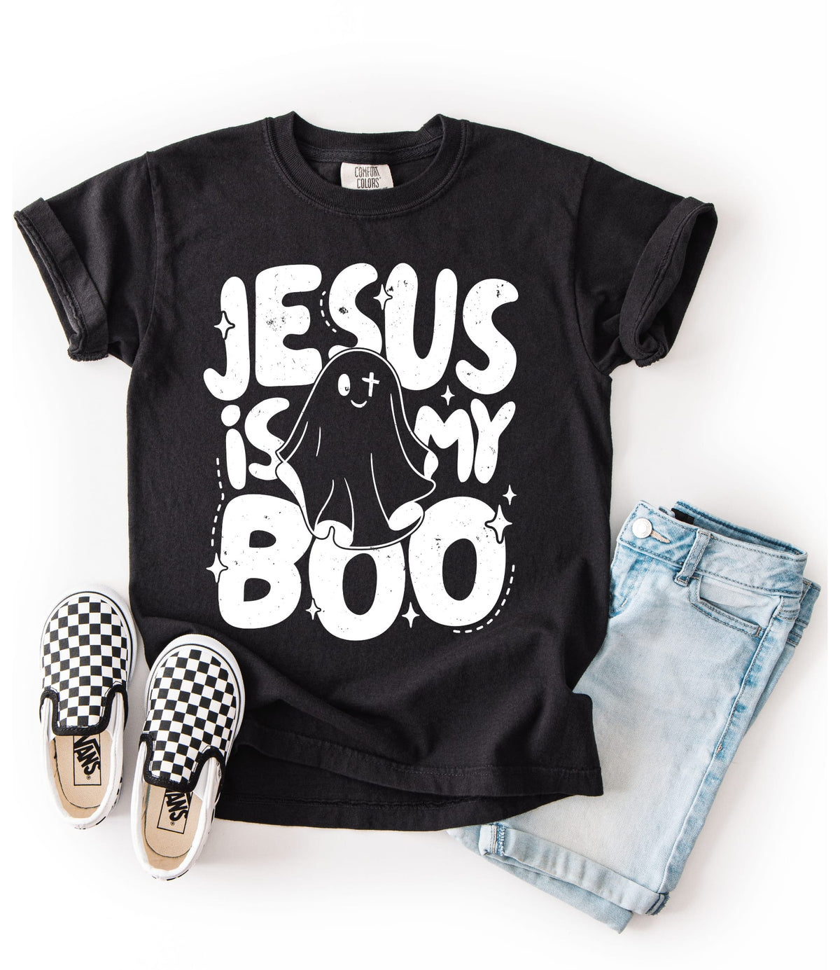A black graphic t-shirt with the text 'JESUS IS MY BOO' and a ghost illustration, styled in a flat lay with light blue denim shorts and black-and-white checkered sneakers on a white background.