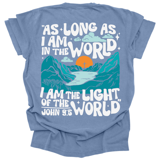 Washed Denim t-shirt featuring a bold mountain and sunrise design with the words "As long as I am in the world, I am the light of the world" from John 9:5.
