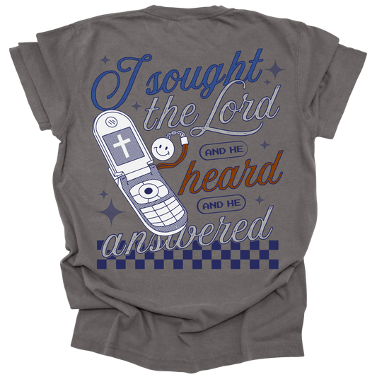 Pepper-colored t-shirt with a retro flip phone graphic and the words "I sought the Lord, and He heard and He answered," inspired by Psalm 34:4, with checkerboard accents.