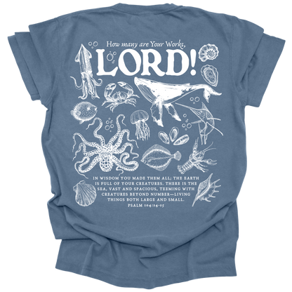 Detailed marine life illustration featuring a humpback whale, jellyfish, octopus, and other sea creatures with the text "How many are Your works, LORD!" and Psalm 104:24-25 on a washed denim Comfort Colors t-shirt.