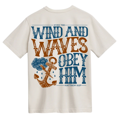 Ivory t-shirt with the words "Even the Wind and Waves Obey Him" in bold, decorative lettering with a stormy anchor graphic, inspired by Matthew 8:27.